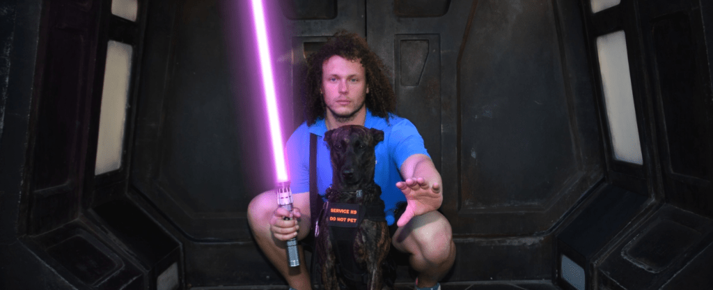 Brannon and his Dutch Shepherd Service Dog, Nala, posing with a lightsaber in a Star Wars-themed photo at Galaxy's Edge in Hollywood Studios, Walt Disney World.